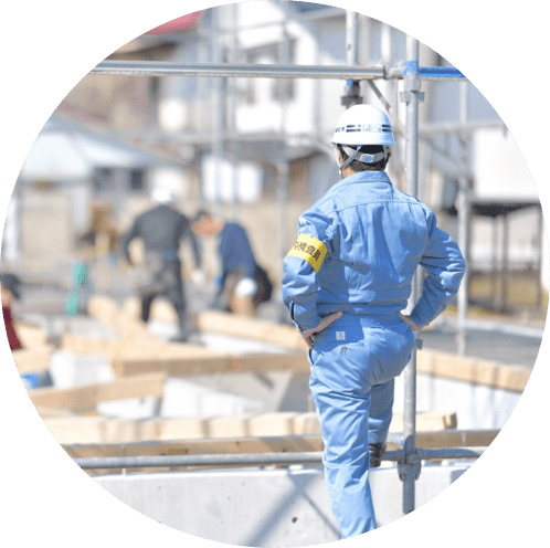 ヘルメッドを被った作業着の男性が腰に手を当てている後ろ姿の写真