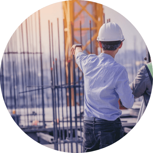 ヘルメッドを被った作業着の男性が指をさしている後ろ姿の写真